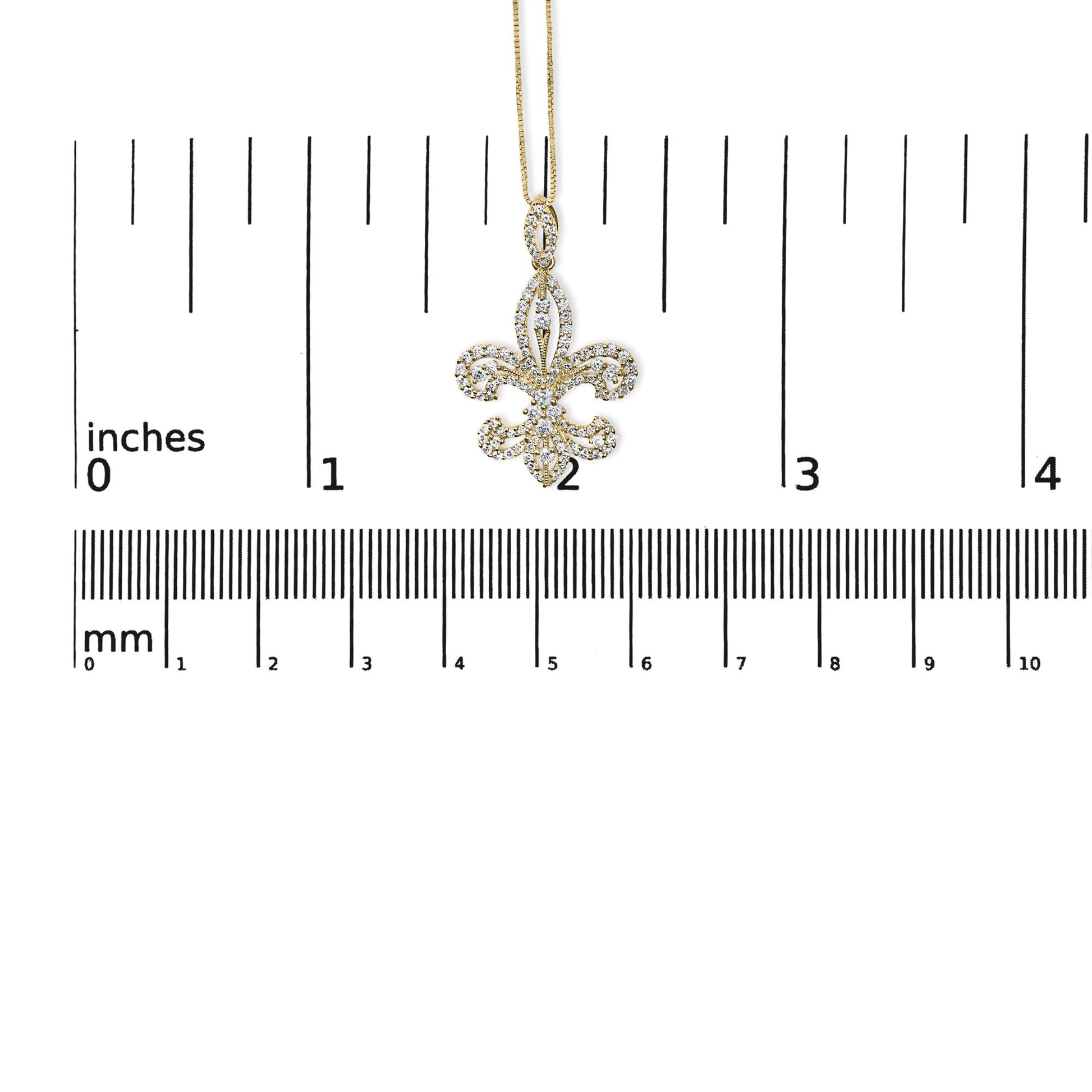 Front view of a yellow metal necklace pendant with white round gemstones in prong settings, shaped like a fleur-de-lis, displayed on a ruler for size reference.