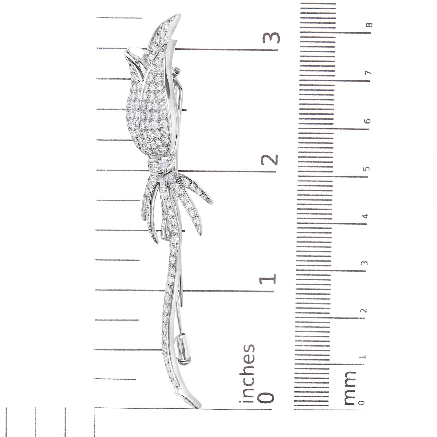 Side view of a white metal flower-shaped brooch with pave-set round white gemstones, placed on a ruler for size reference.