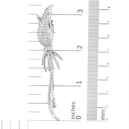 Side view of a white metal flower-shaped brooch with pave-set round white gemstones, placed on a ruler for size reference.