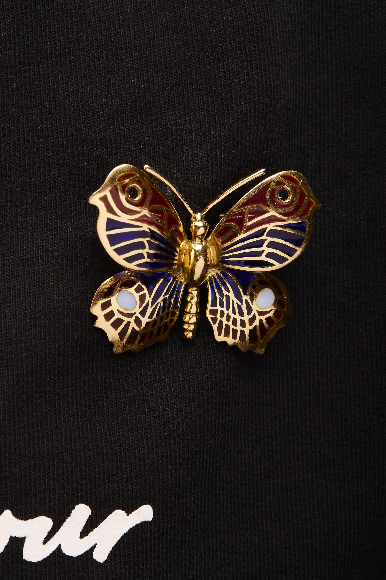 Yellow metal butterfly-shaped brooch with blue, red, and white gemstone accents, shown from the front on black fabric.