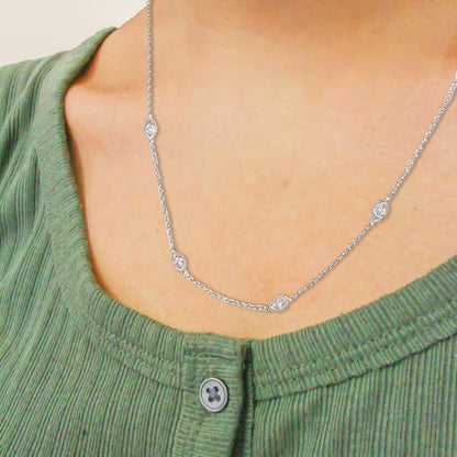 Close-up front view of a white metal necklace on a model, featuring round white gemstones in bezel settings evenly spaced along the chain.