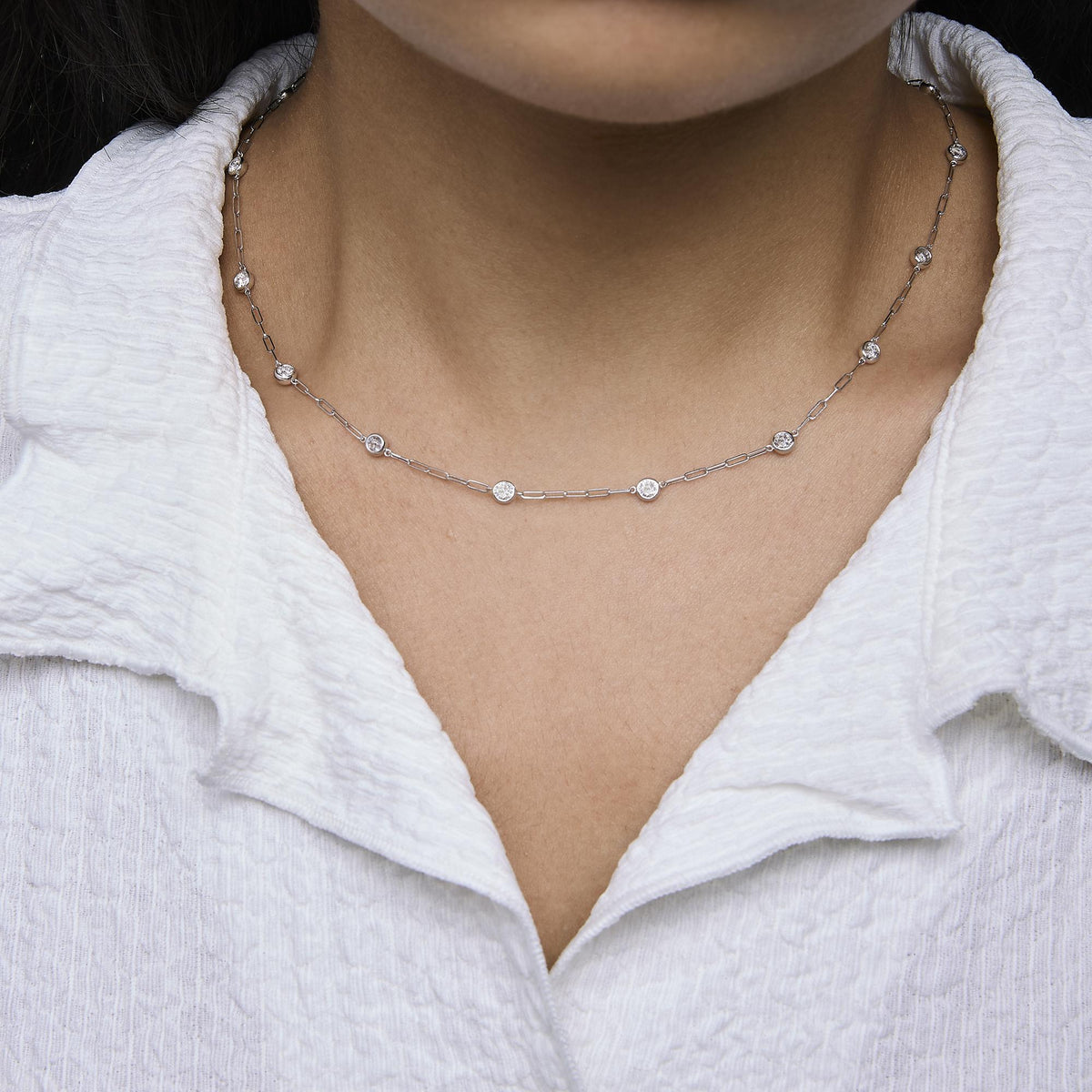 White metal necklace with round bezel-set white gemstones evenly spaced along a fine link chain, shown worn on a model, close-up front angle.