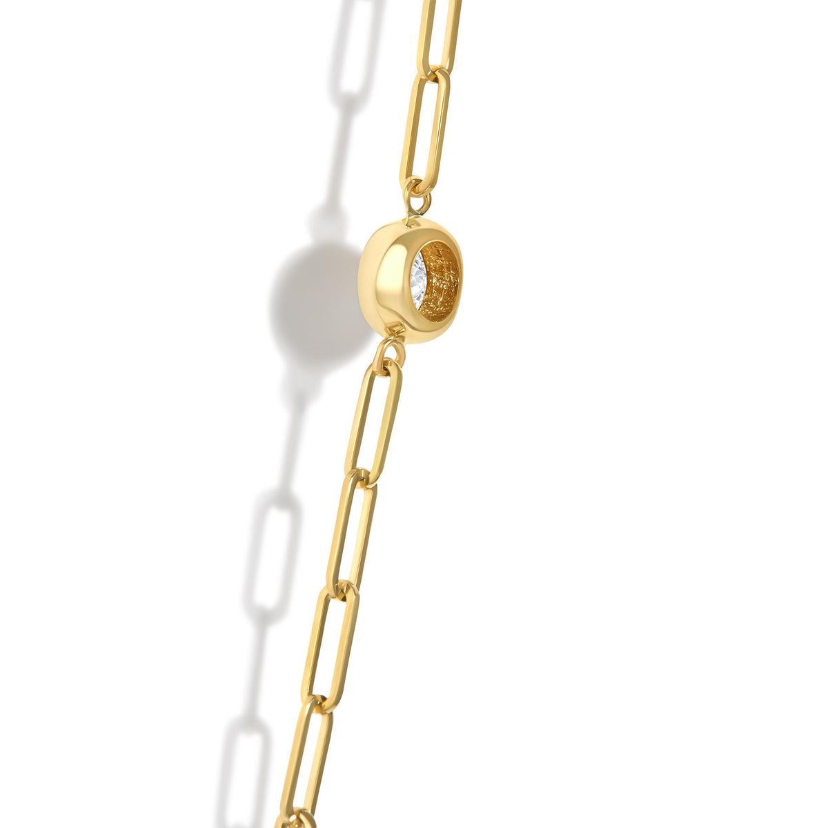 Close-up angled view of a yellow metal necklace chain featuring a round bezel-set white gemstone pendant, shown on a white background.