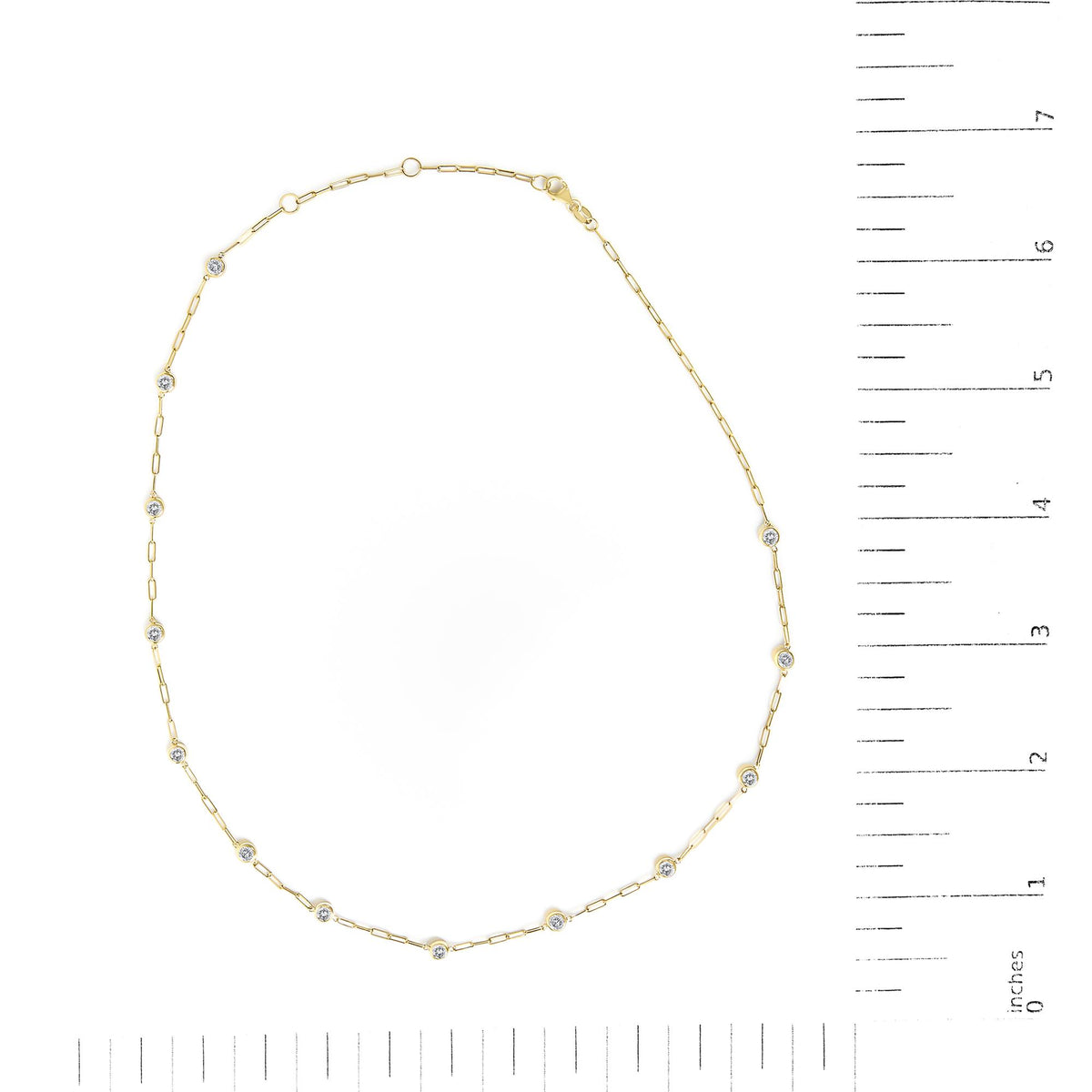 Yellow necklace with small bezel set round white gemstones linked by thin chain, shown flat on a scale from above.