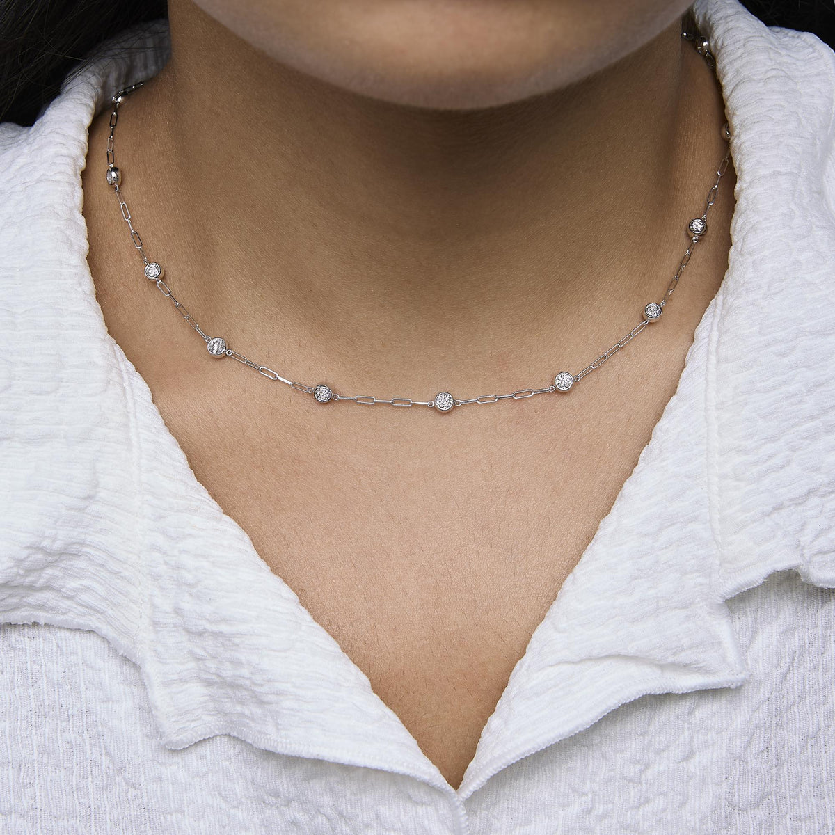 Close up front view of 14K Gold 2.0 cttw round diamond bezel set paperclip station necklace on a model in a white blouse