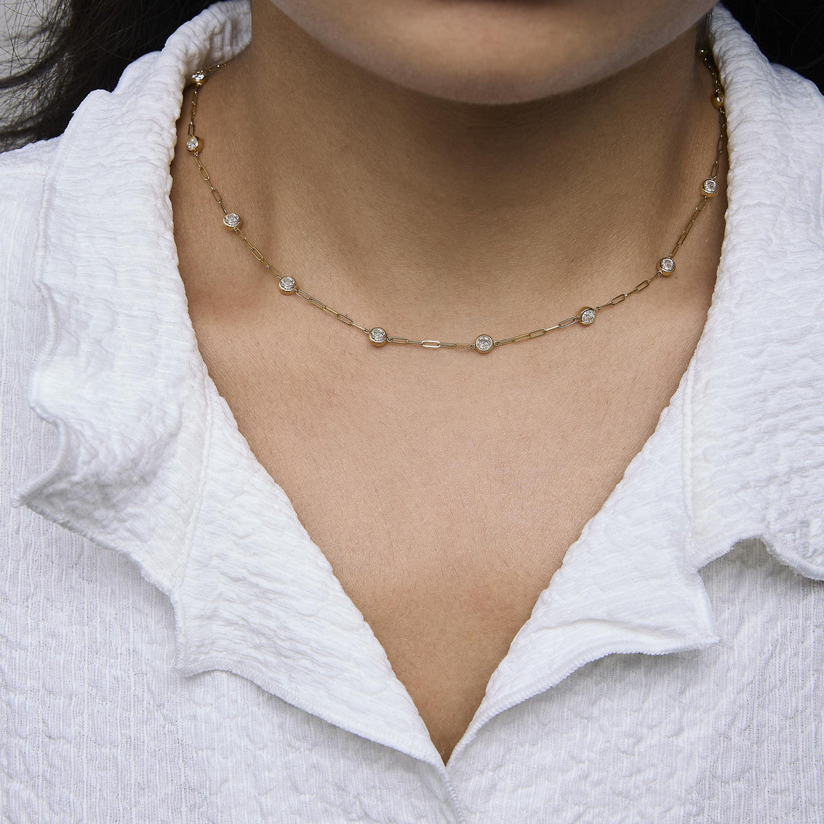 Close-up front view of a yellow metal necklace with round white gemstones in bezel settings, shown worn on a model.