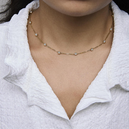 Close-up front view of a yellow metal necklace with round white gemstones in bezel settings, shown worn on a model.