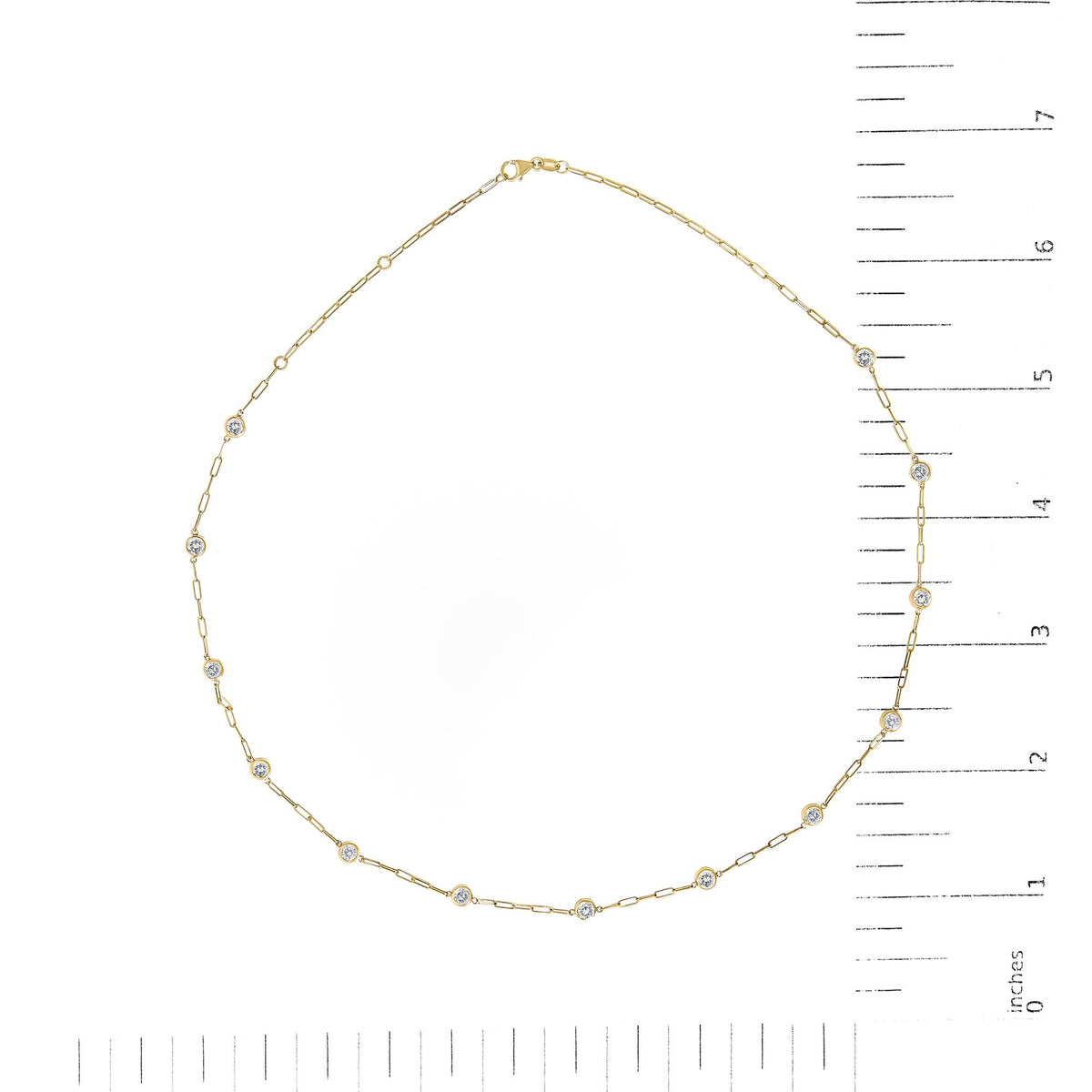 Close-up top view of a yellow metal necklace with round white gemstones set in bezel settings along the chain, shown on a measurement scale.