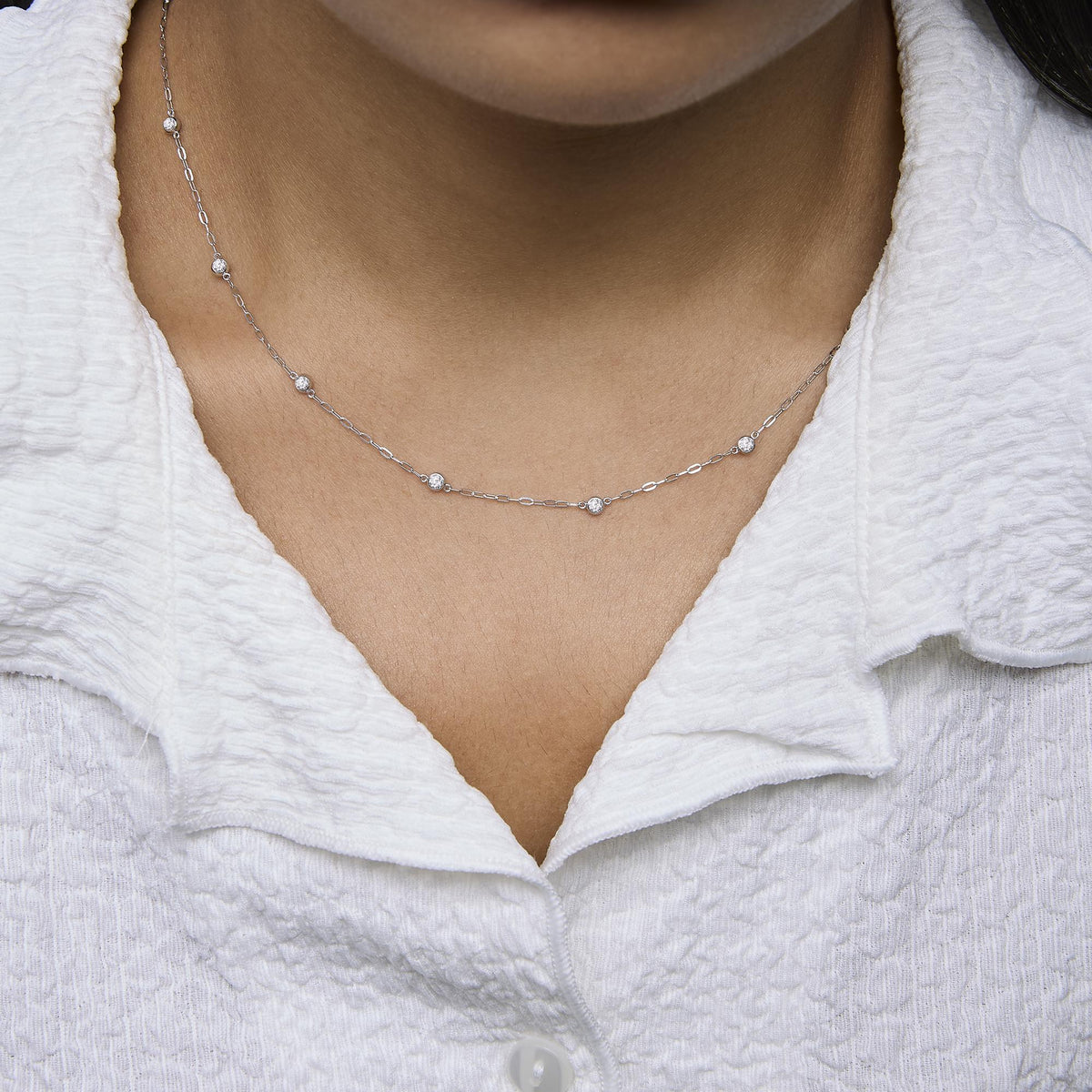 White metal necklace with small round white gemstones in bezel settings, shown worn on a model, close-up front angle.