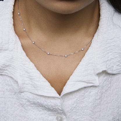 White metal necklace with small round white gemstones in bezel settings, shown worn on a model, close-up front angle.