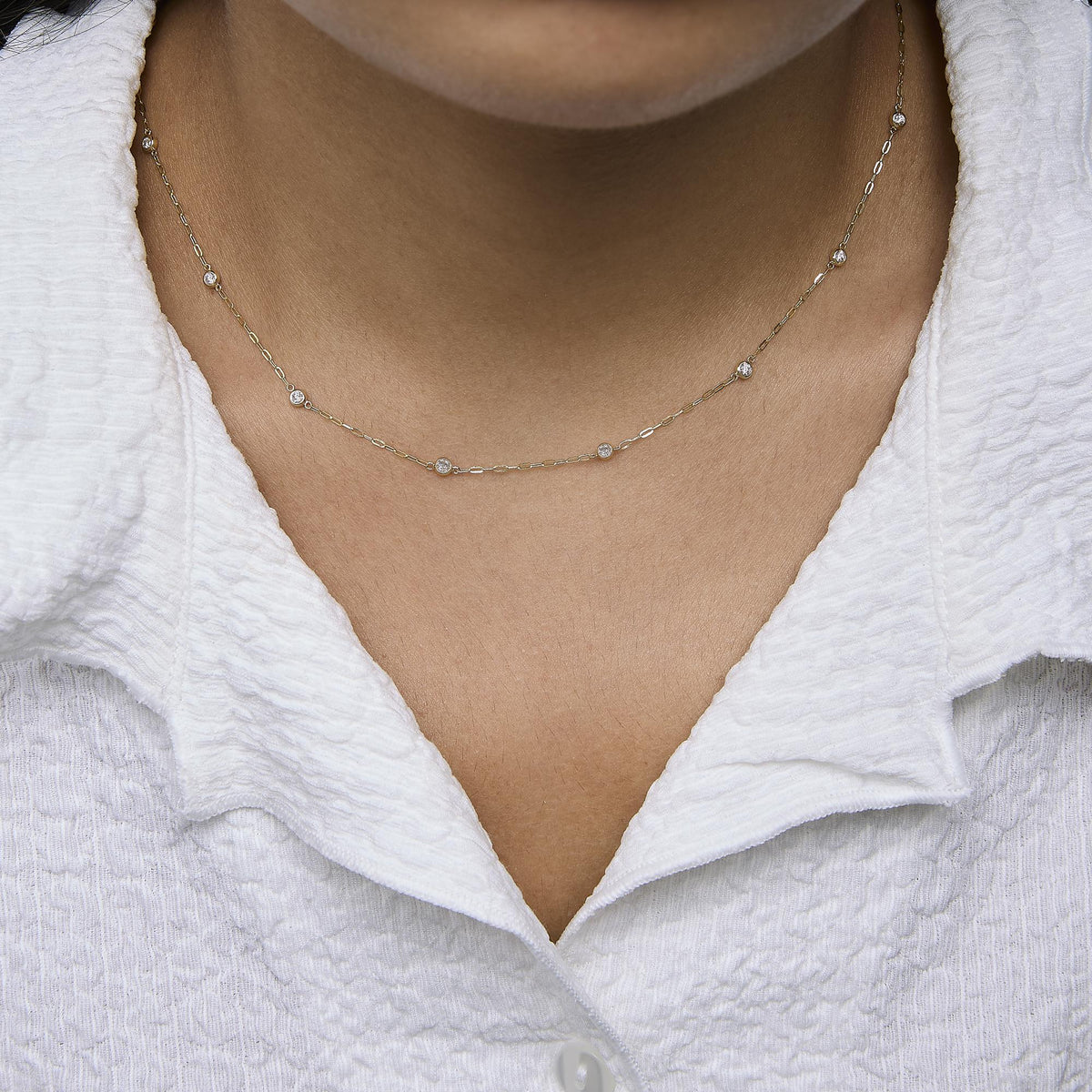 Yellow metal necklace with round white gemstones in bezel settings spaced along a delicate chain, shown worn on a model, front close-up angle.