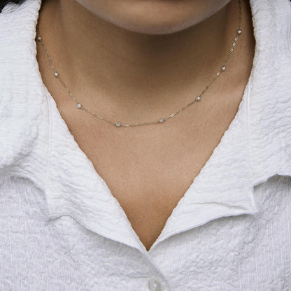 Yellow metal necklace with round white gemstones in bezel settings spaced along a delicate chain, shown worn on a model, front close-up angle.