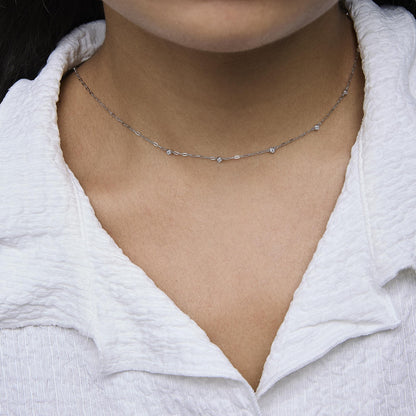 Close-up front view of a model wearing a delicate white necklace with round bezel-set white gemstones evenly spaced along the chain.