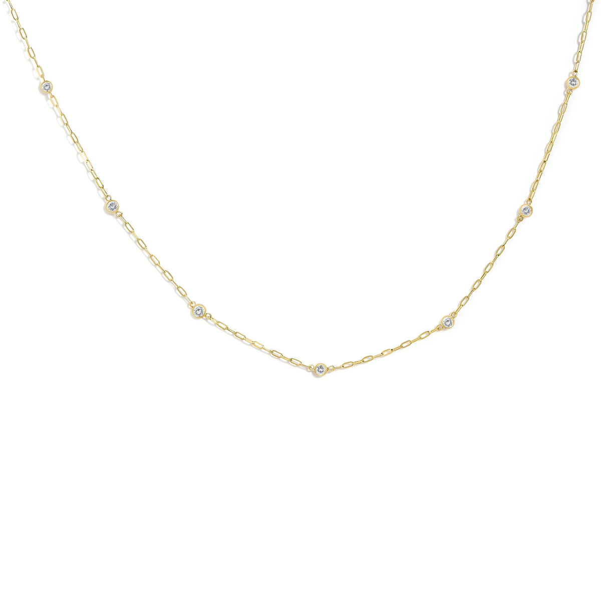 Close-up front angle of a yellow metal necklace featuring round white gemstones in bezel settings spaced evenly along a delicate chain.