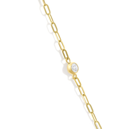 Close-up angled view of a yellow metal necklace chain with a bezel-set white round gemstone pendant.