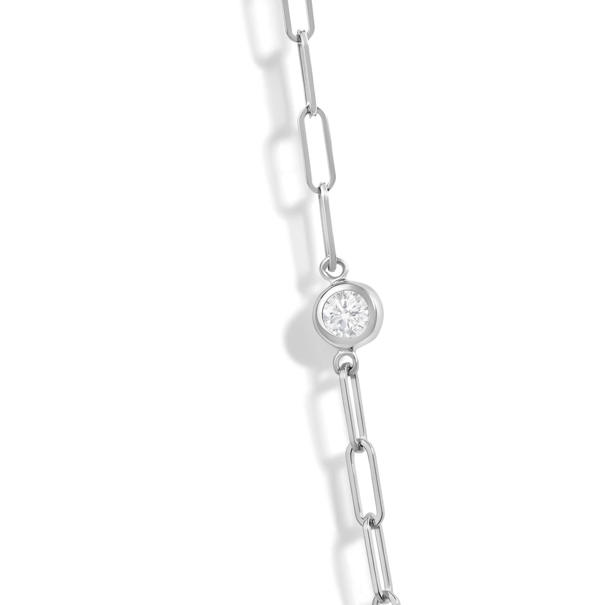 Close-up angled view of a white metal necklace chain with bezel-set round white gemstones.