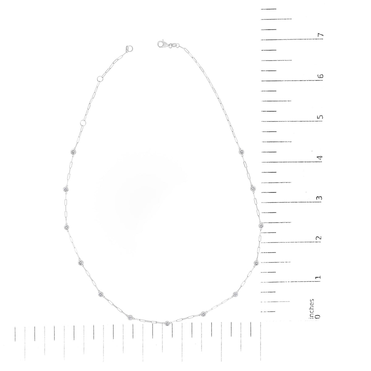 White metal necklace with round white gemstones in bezel settings evenly spaced along a delicate chain, shown on a ruler scale photographed from above.