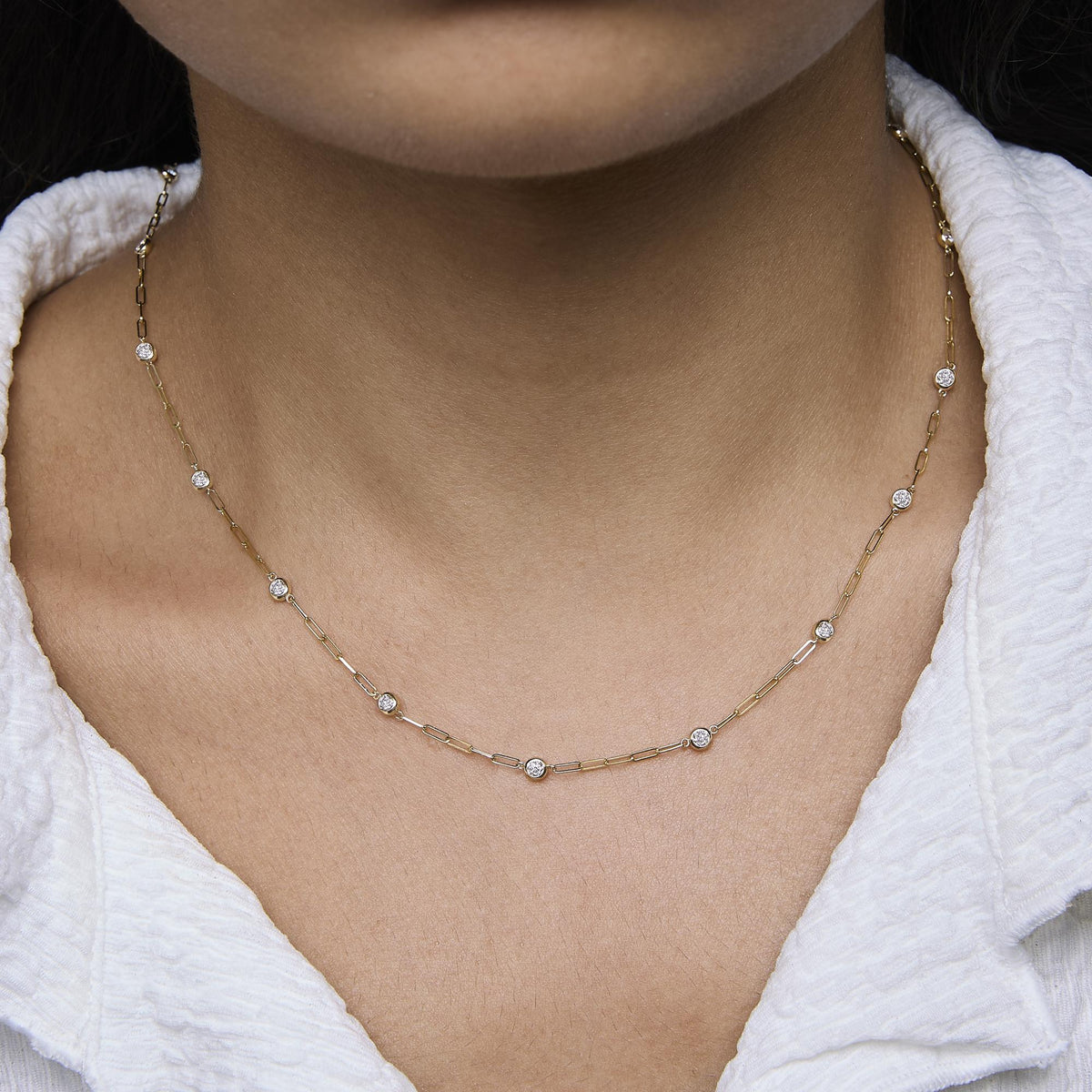Close-up front view of a model wearing a yellow necklace with round white gemstones in bezel settings spaced along a chain.