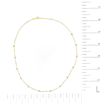 Top view of a yellow necklace with round white gemstones in bezel settings along the chain, shown on a scale.