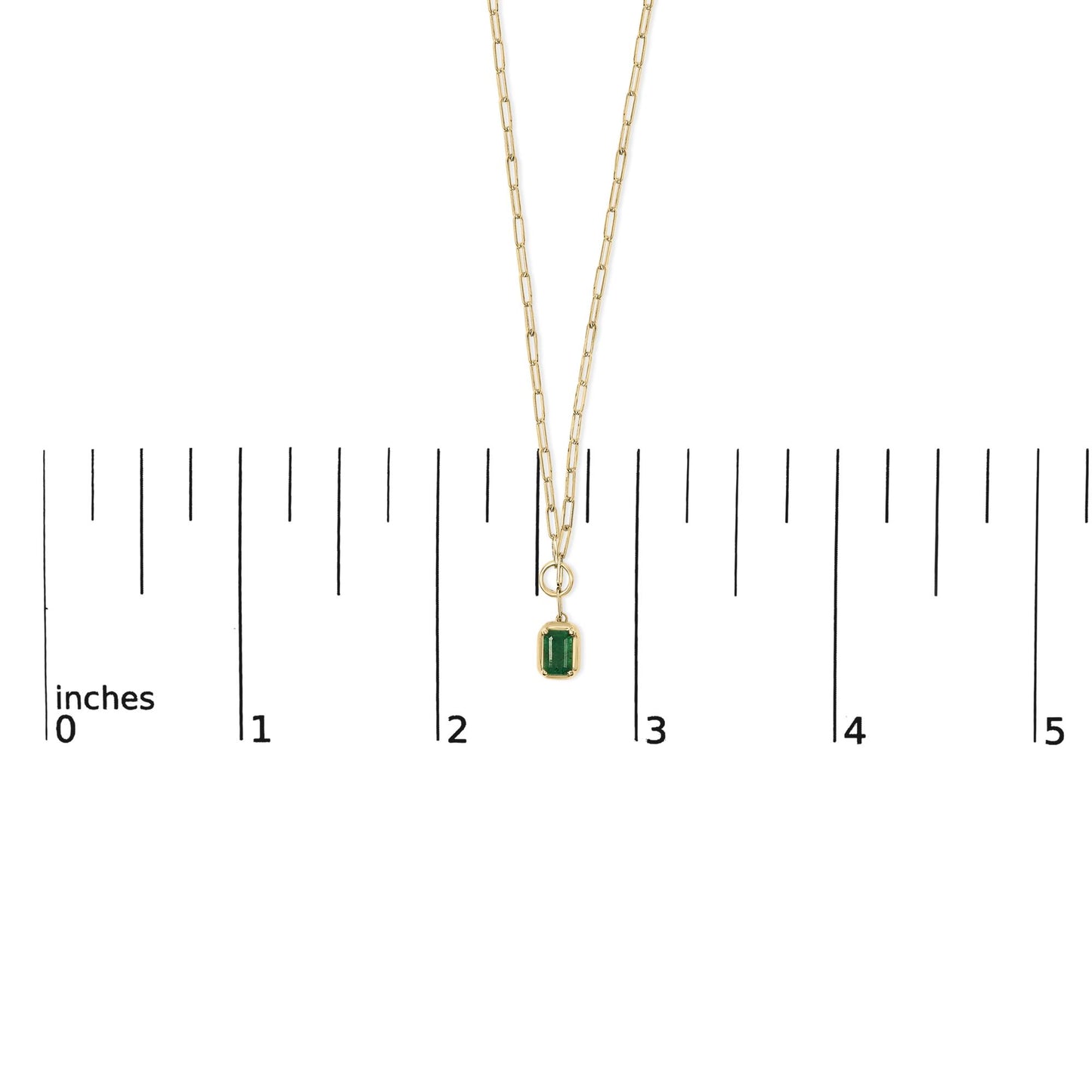 Yellow metal necklace with a green emerald-shaped gemstone in bezel setting, shown on a scale from above.