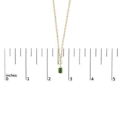Yellow metal necklace with a green emerald-shaped gemstone in bezel setting, shown on a scale from above.