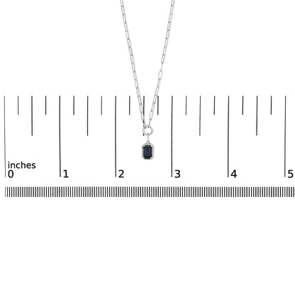 White metal necklace with a blue emerald-shaped gemstone pendant in bezel setting, shown on a ruler scale, front view.