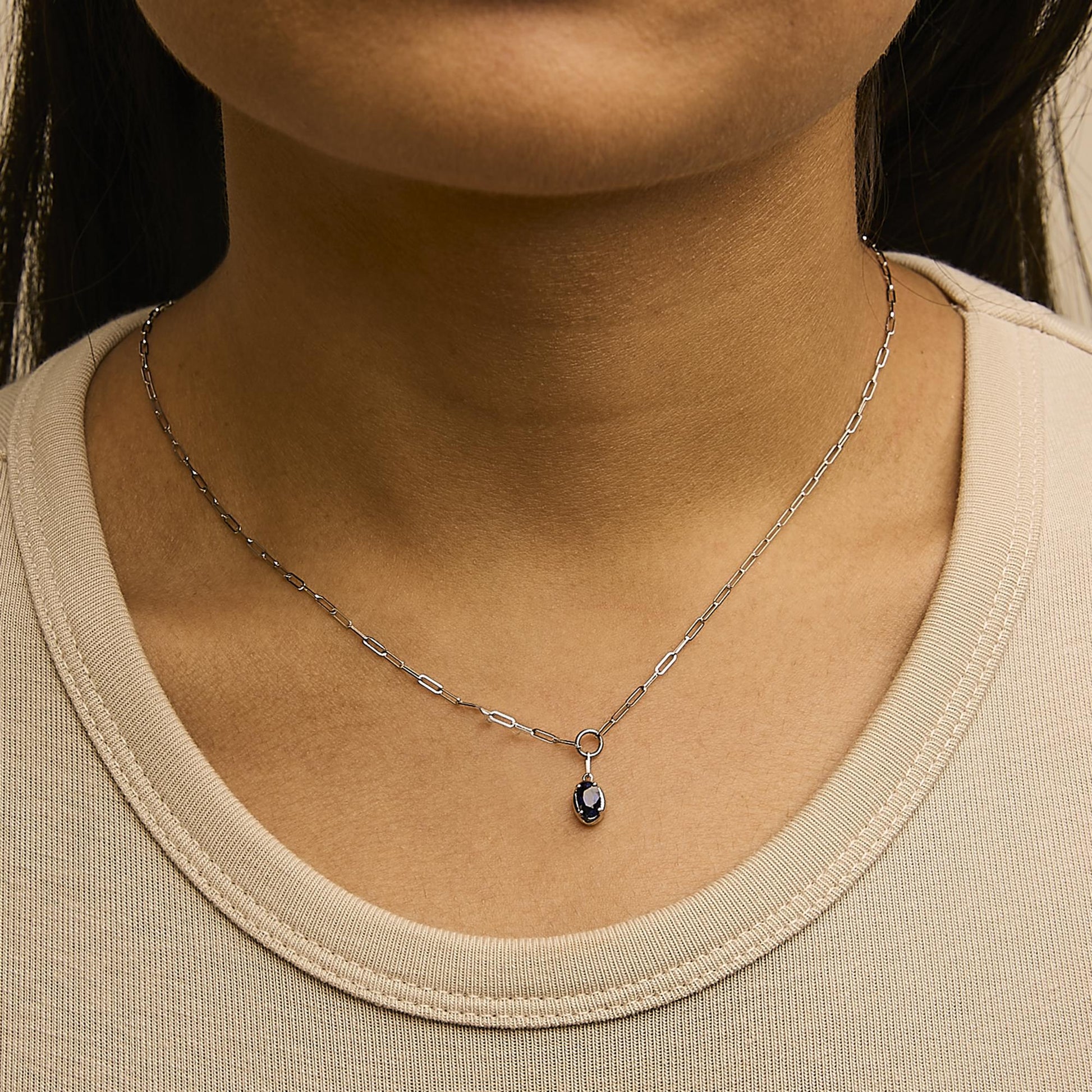 Close-up front view of a model wearing a white metal necklace with an oval blue gemstone pendant on a delicate chain.