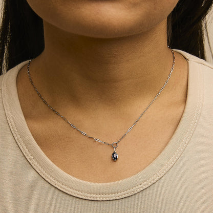 Close-up front view of a model wearing a white metal necklace with an oval blue gemstone pendant on a delicate chain.