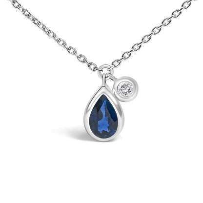 Close-up front view of a white metal necklace with two bezel-set pendants: one pear-shaped blue gemstone and one round white gemstone.