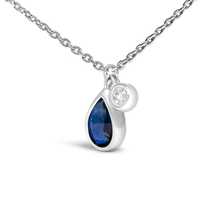 Close-up front angle of a white necklace featuring a pear-shaped blue gemstone and a smaller round white gemstone, both bezel set, hanging side by side on a chain.