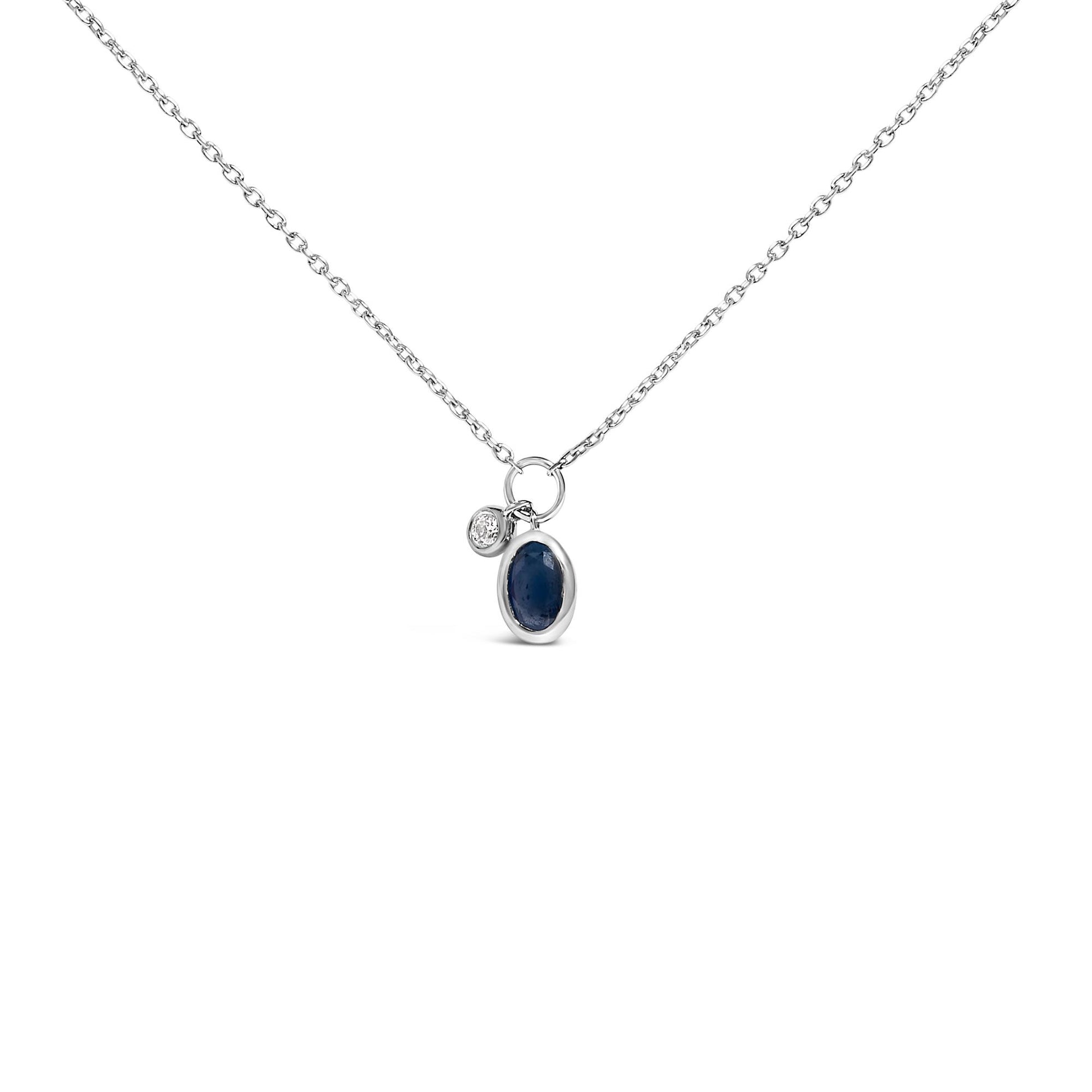 Front-facing shot of a white chain necklace with two small bezel-set pendants, one oval-shaped blue gemstone and one round white gemstone.