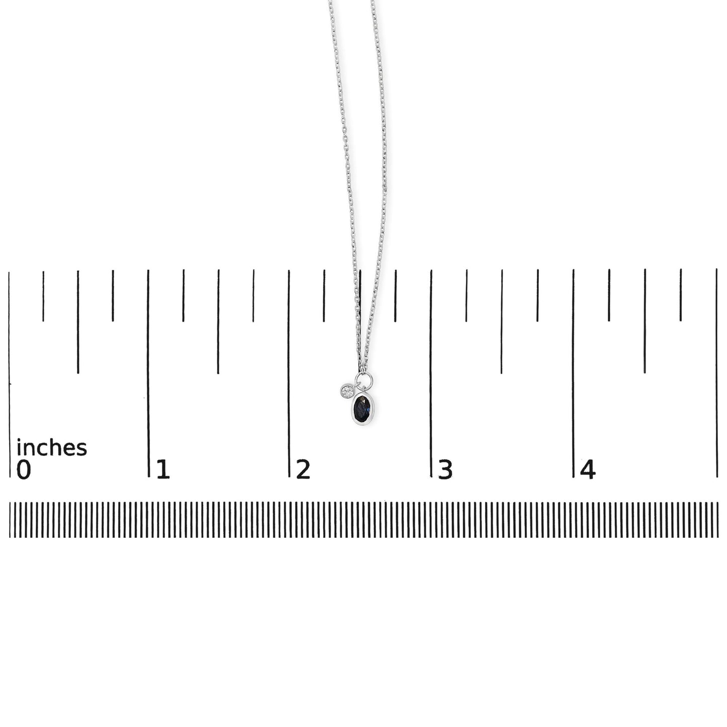 White necklace with an oval blue gemstone and a round white gemstone pendant in bezel settings, shown hanging on a scale with an overhead view.