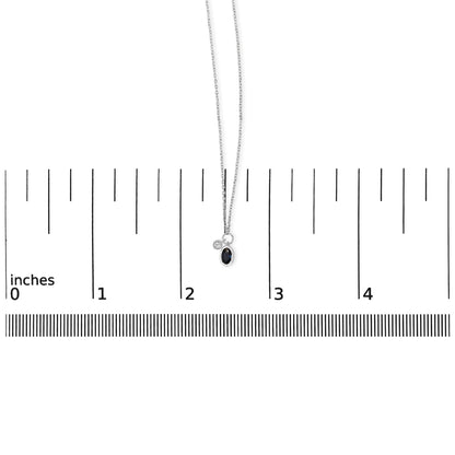 White necklace with an oval blue gemstone and a round white gemstone pendant in bezel settings, shown hanging on a scale with an overhead view.