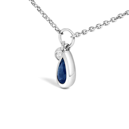 Close-up front angle of a white metal necklace with a pear-shaped blue gemstone pendant and a small round white gemstone, both in bezel settings.