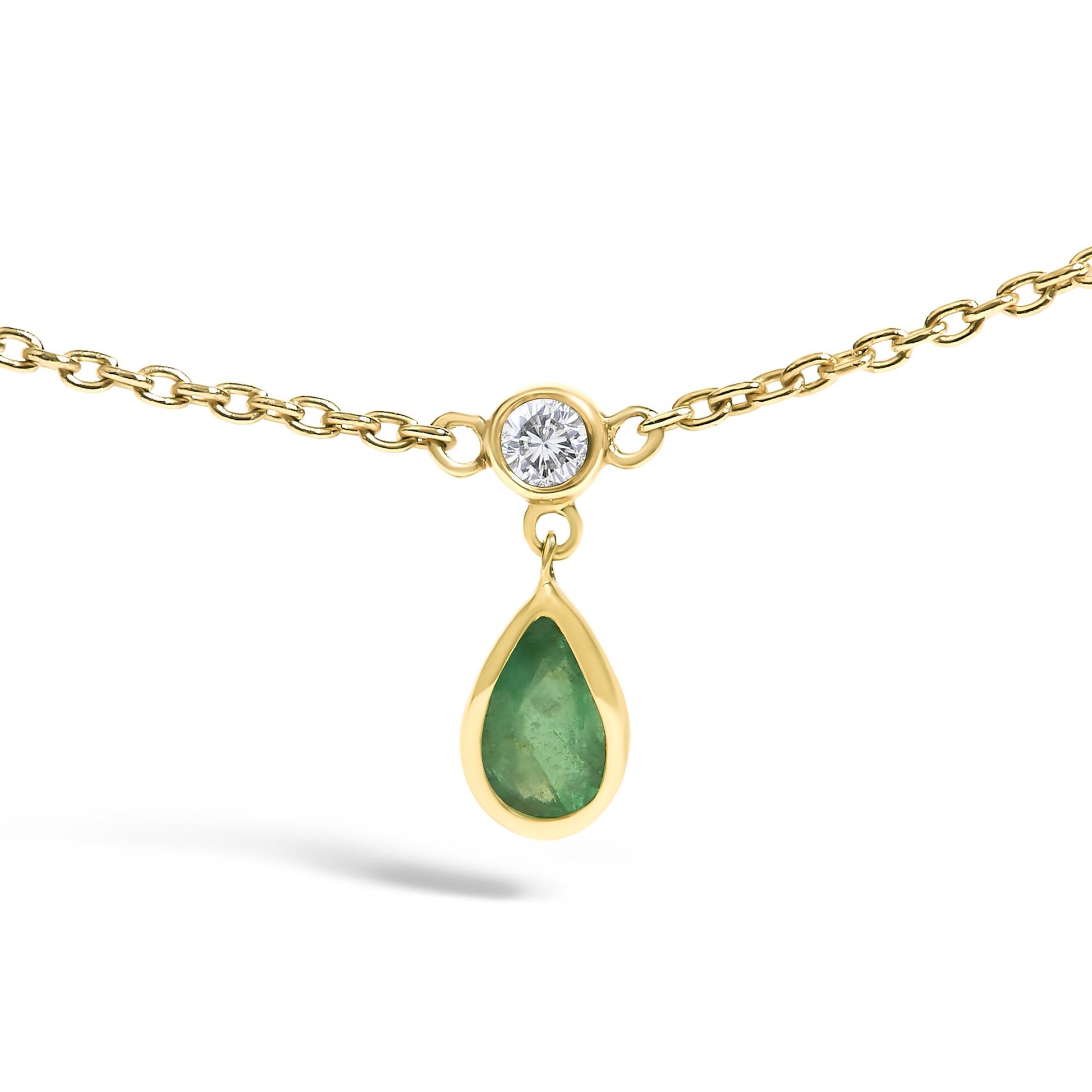 Close-up front view of a yellow necklace with a small round white gemstone in a bezel setting connected to a dangling pear-shaped green gemstone also in a bezel setting.