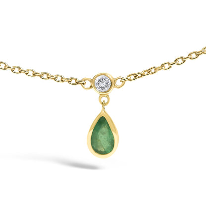 Close-up front view of a yellow necklace with a small round white gemstone in a bezel setting connected to a dangling pear-shaped green gemstone also in a bezel setting.
