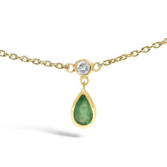 Close-up front view of a yellow necklace with a small round white gemstone in a bezel setting connected to a dangling pear-shaped green gemstone also in a bezel setting.