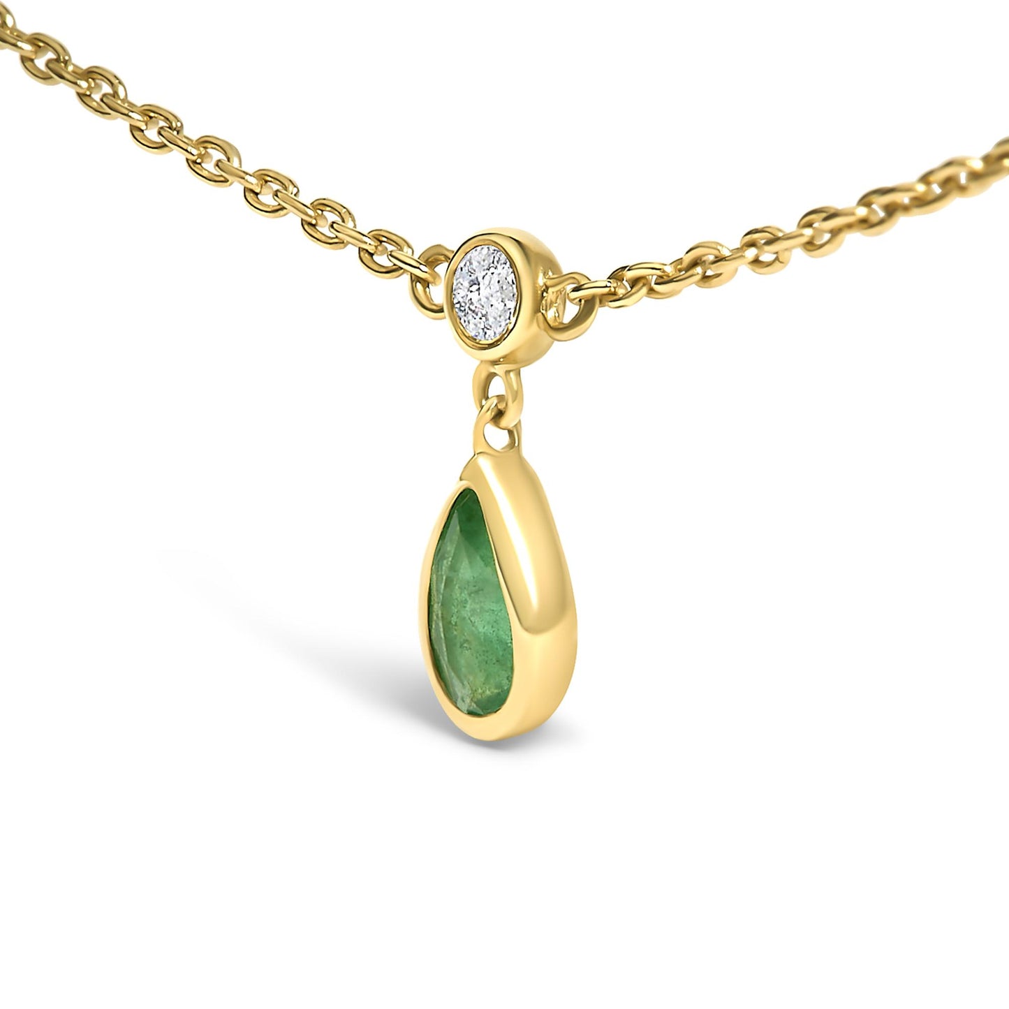 Close-up angled view of a yellow metal necklace chain with a pear-shaped green gemstone pendant bezel set, hanging below a round white gemstone also bezel set.