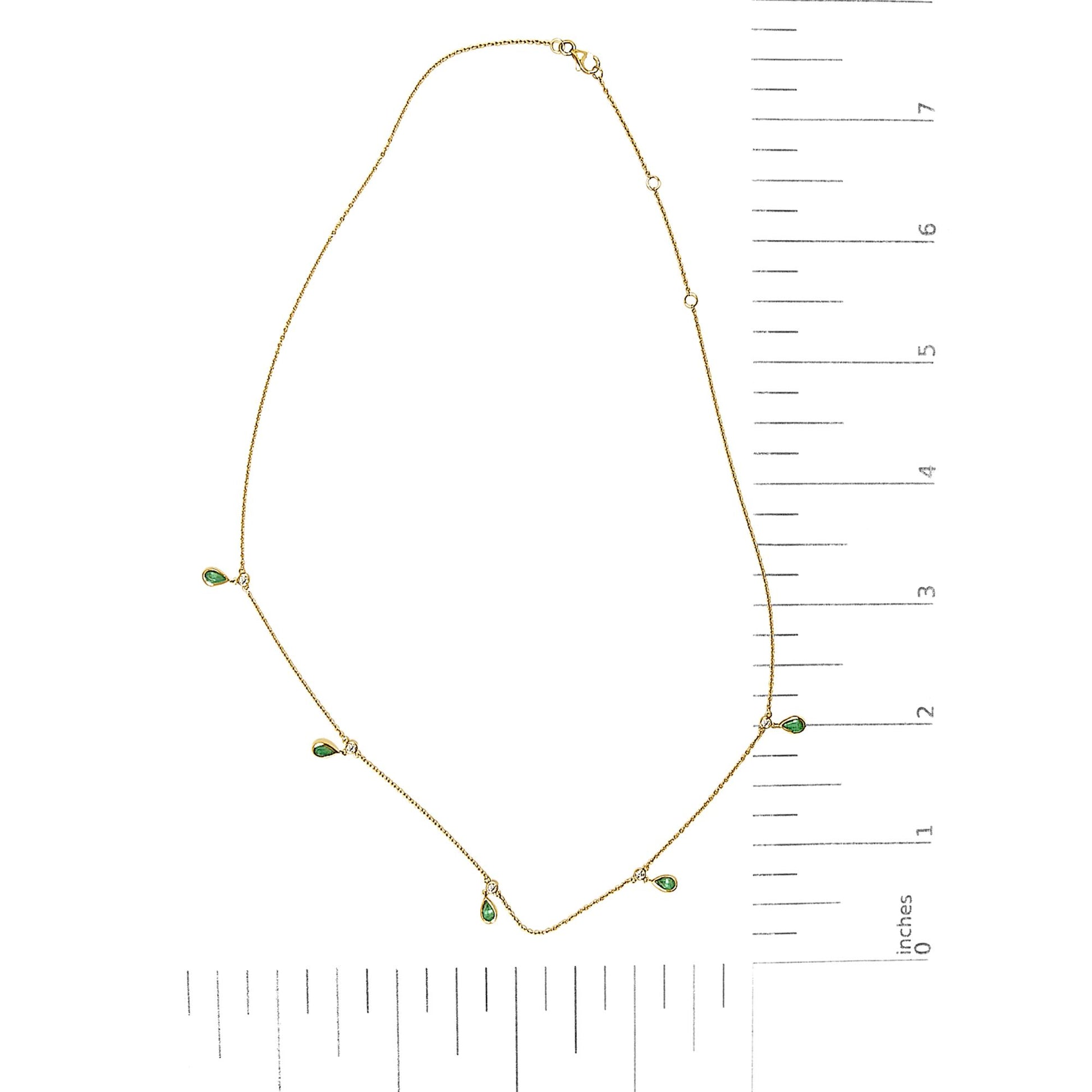 Yellow necklace with small pear-shaped green gemstones and round white gemstones in bezel settings, shown on a ruler scale from a top-down angle.