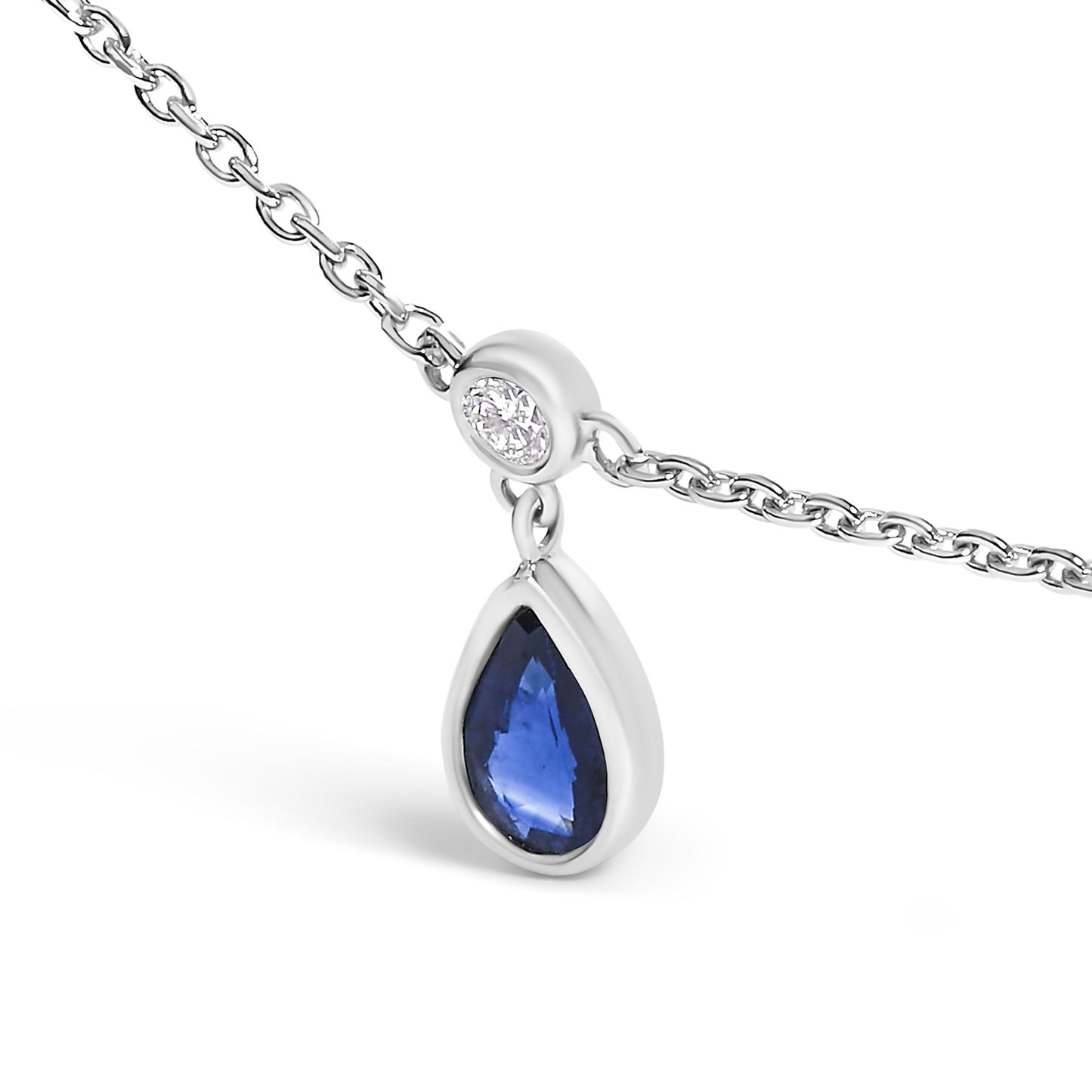 Close-up front angle of a white metal necklace chain with a pendant featuring a round white gemstone in bezel setting above a pear-shaped blue gemstone in bezel setting.