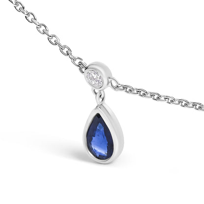 Close-up front angle of a white metal necklace chain with a pendant featuring a round white gemstone in bezel setting above a pear-shaped blue gemstone in bezel setting.
