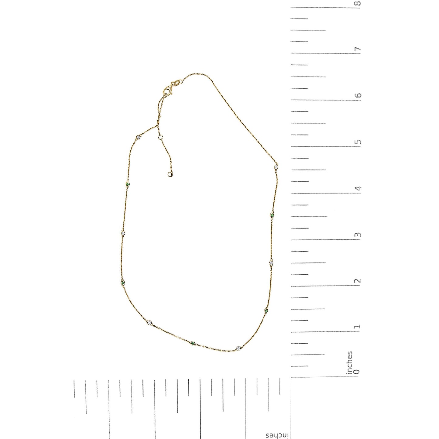 Yellow metal necklace shown flat on a scale with round white and green gemstones in bezel settings spaced along the chain.
