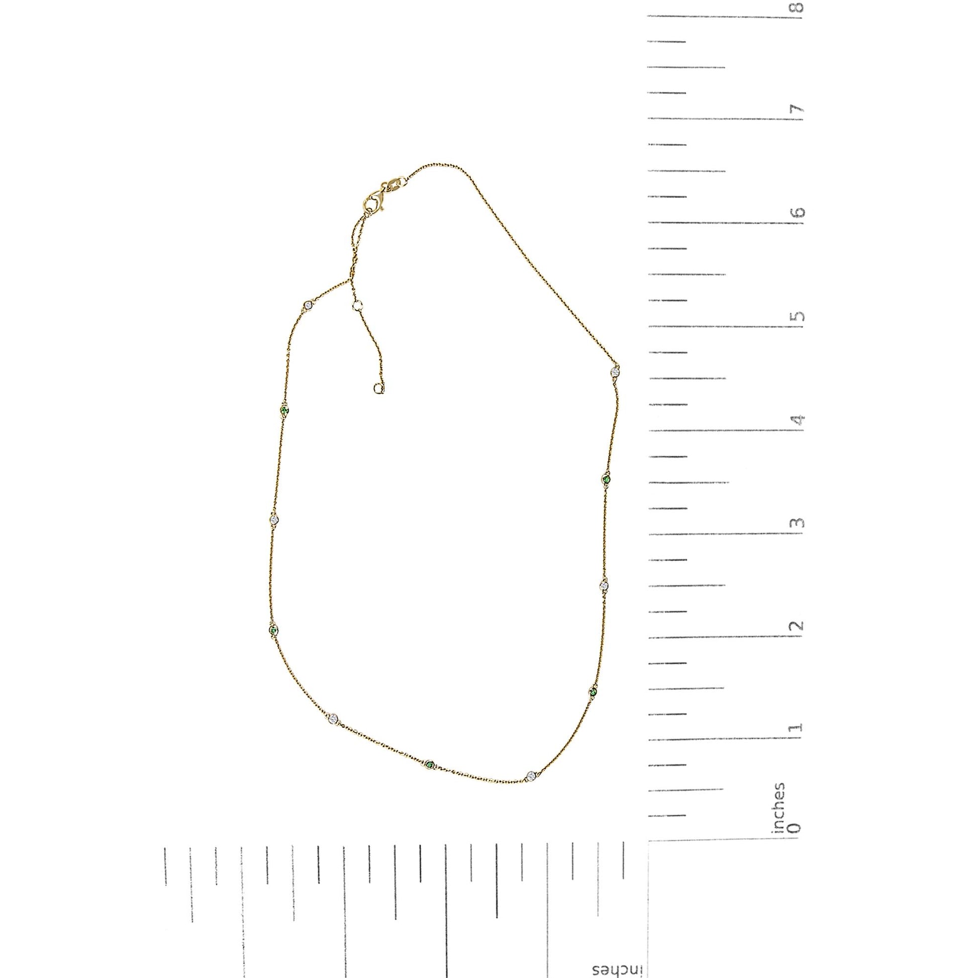 Yellow metal necklace shown flat on a scale with round white and green gemstones in bezel settings spaced along the chain.