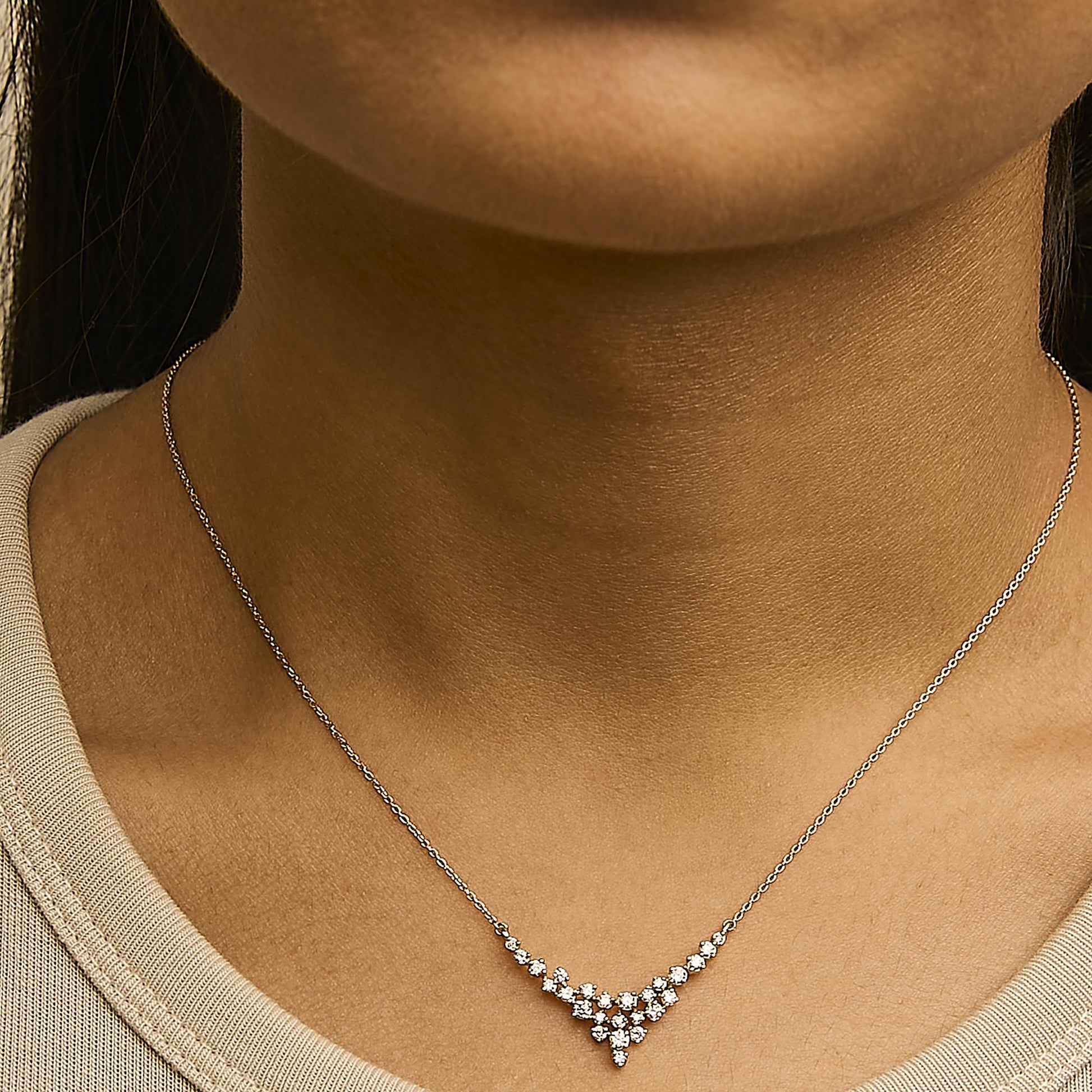 Close-up front view of a yellow metal necklace with a cluster of white round gemstones in prong settings, shown worn on a model.