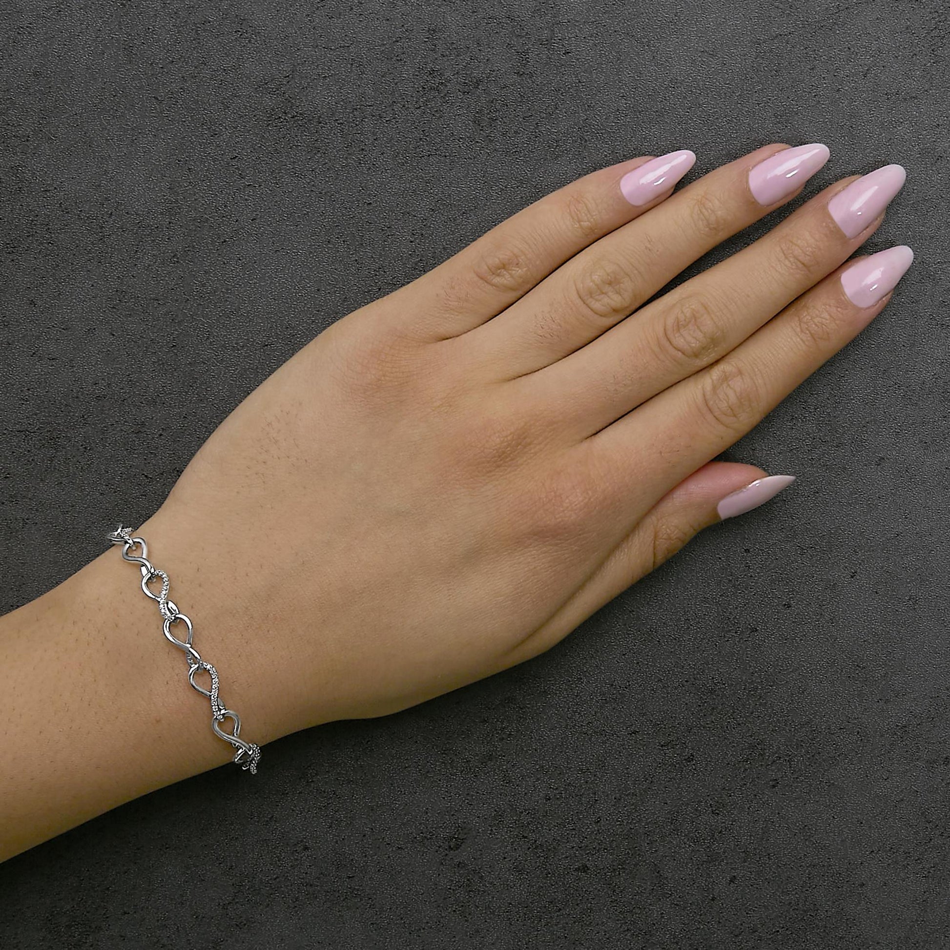 White metal bracelet with alternating smooth and white gemstone-encrusted infinity shapes, shown on a model's wrist in a top-down angle.