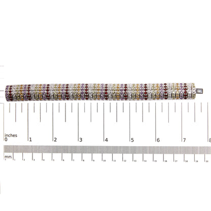 Top-down view of a white metal bracelet with multiple rows of round purple, blue, lemon, yellow, and red gemstones in shared prong settings, placed on a ruler for size reference.