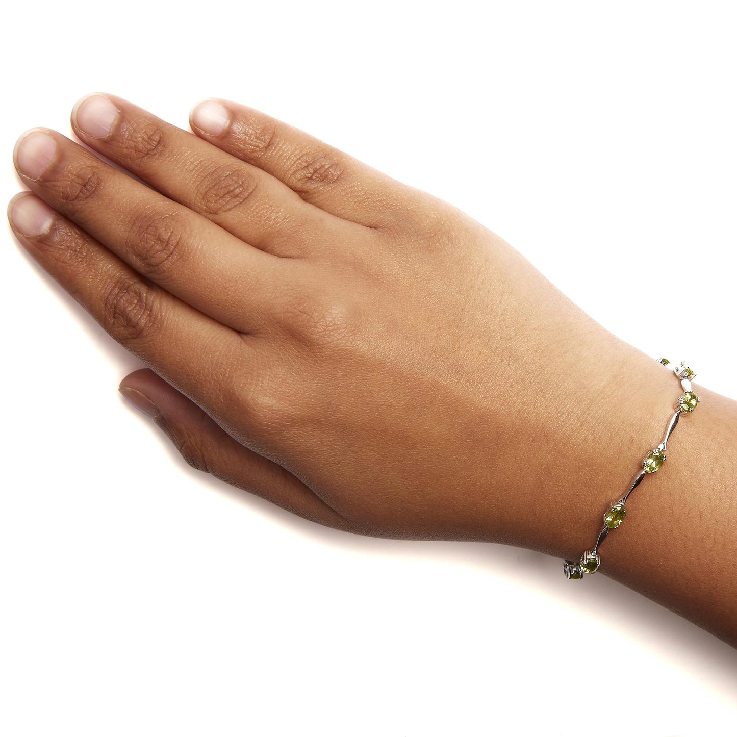 White metal bracelet with oval green gemstones in 4-prong settings, shown on a model's wrist from a top-down angle.