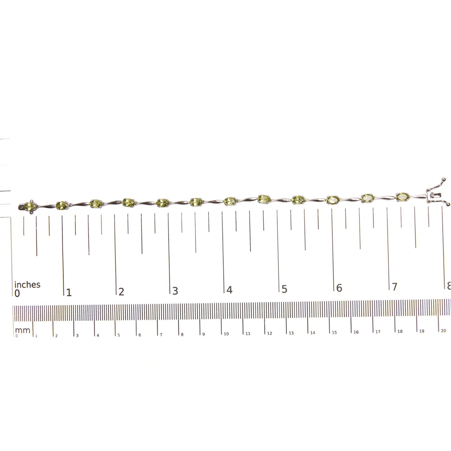 White metal bracelet with oval green gemstones in 4-prong settings, laid flat on a ruler for size reference, shot from above.