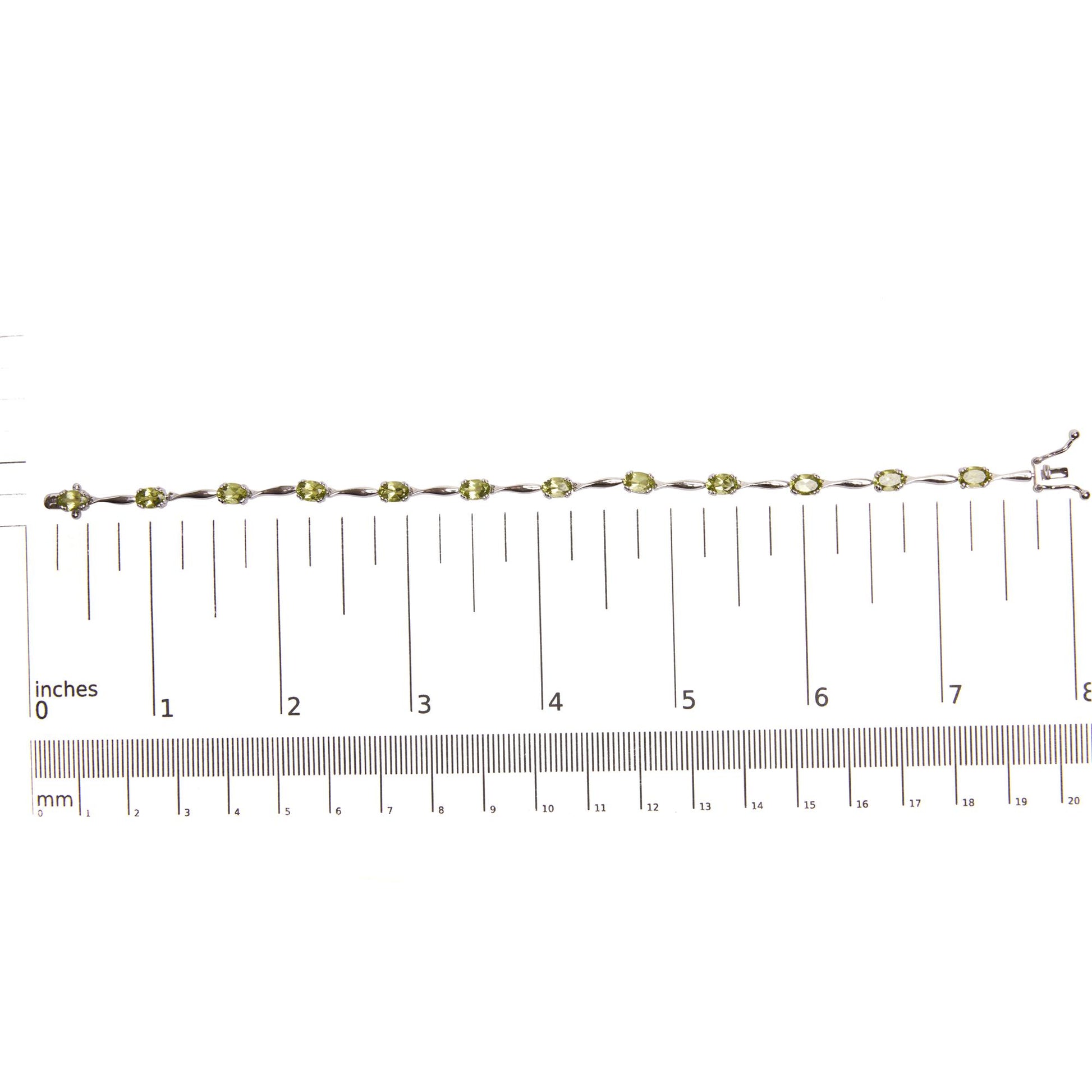 White metal bracelet with oval green gemstones in 4-prong settings, laid flat on a ruler for size reference, shot from above.