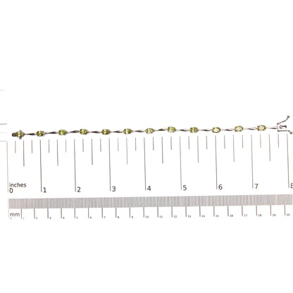 White metal bracelet with oval green gemstones in 4-prong settings, laid flat on a ruler for size reference, shot from above.